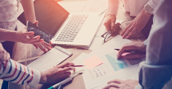 A group of coworkers sit at a desk researching CME marketing techniques