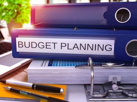 Blue Ring Binder with Inscription Budget Planning on Background of Working Table with Office Supplies and Laptop. Budget Planning Business Concept on Blurred Background